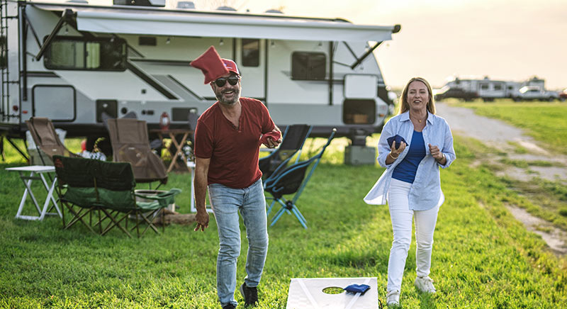 Photo of a couple playing games at a campground with a Jay Feather travel trailer in the background.