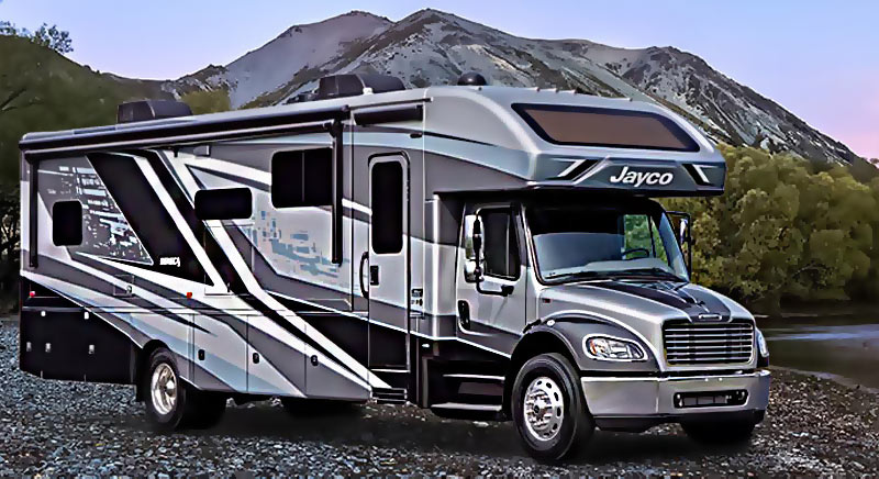 Photo of a Jayco Seneca super-C motorhome on a rocky beach with mountains in the background.