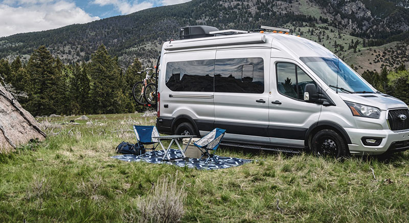 Photograph of a couple barbecuing with a Jayco Solstice camper van in the background.