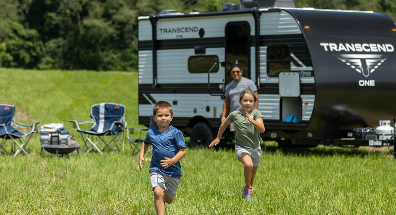 Photo of family playing outside with Grand Design Transcend ONE travel trailer in the background.